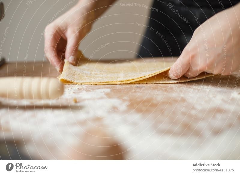 Crop person preparing making pasta with elastic dough fold layer cook roll flour prepare kitchen ingredient process table utensil food cuisine culinary homemade