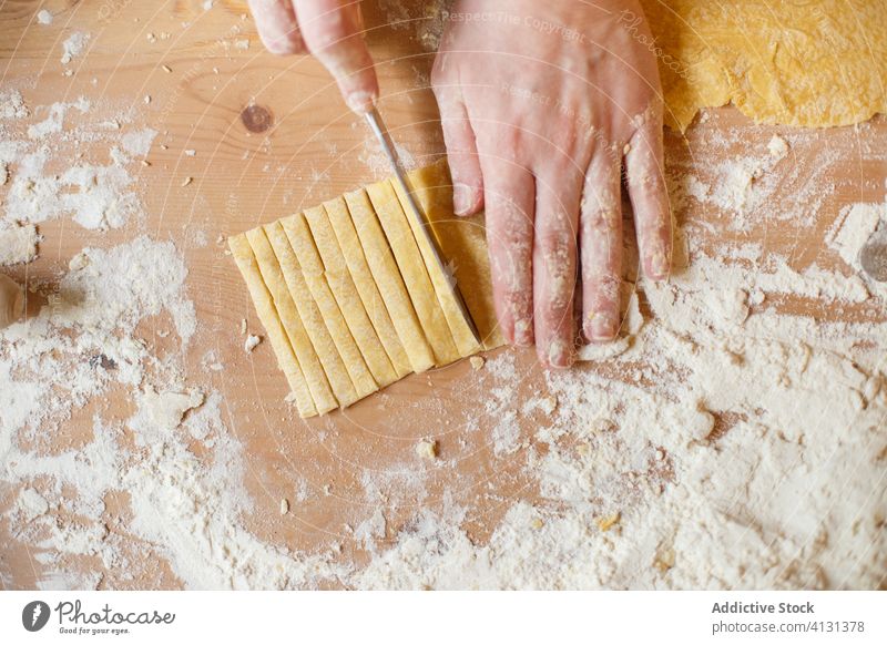 Unrecognizable person cutting pasta dough on table homemade stripe cook thin knife flour prepare kitchen roll process food cuisine culinary recipe handmade chef