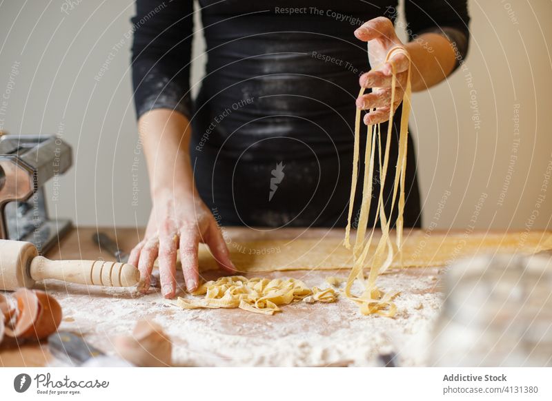 Unrecognizable woman with cut raw pasta homemade dough strap thin stripe pastry cook table flour kitchenware roll eggshell prepare ingredient process