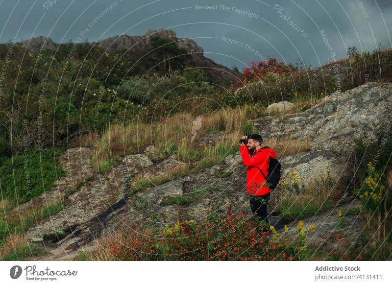 Male hiker taking photos standing on rocky cliff on cloudy day man tourist photographer take photo hill nature overcast gloomy storm explore adventure memory