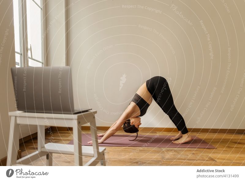 Calm woman standing in downward dog pose while doing yoga stretch flexible healthy lifestyle home laptop tutorial online balance fit vitality workout using
