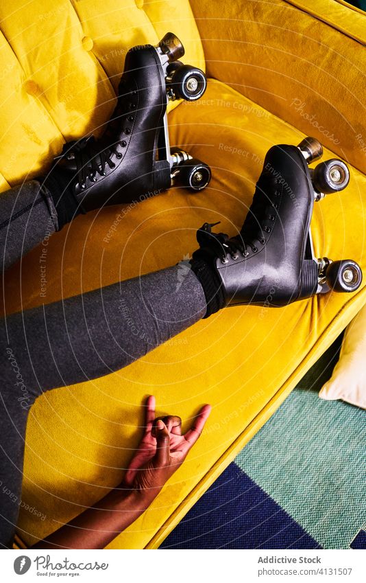 Anonymous woman in roller skates lying on sofa stay home activity colorful gesture rock young black horn female african american concept restriction isolation