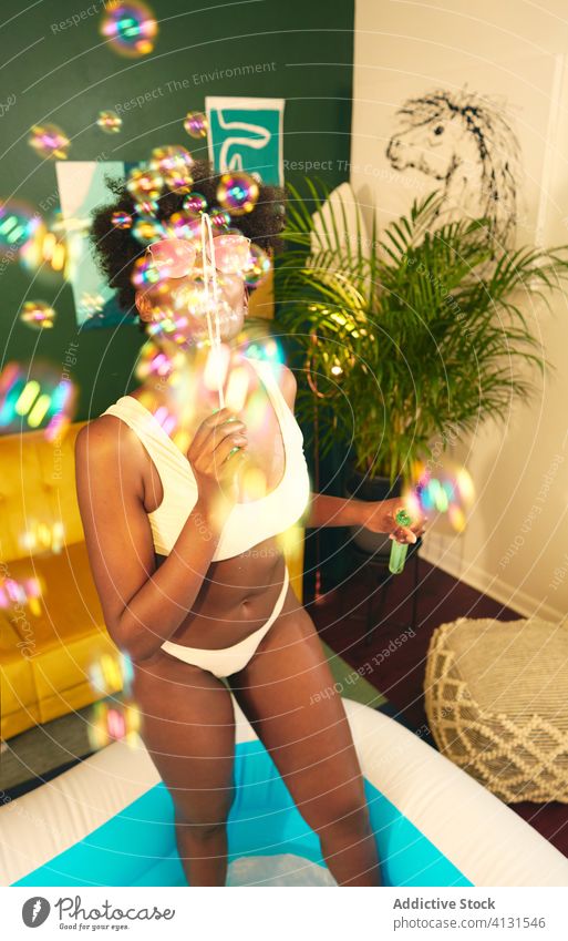 Black woman blowing bubbles in living room pool stay at home social distancing inflatable soap bubble self isolation weekend party having fun female ethnic