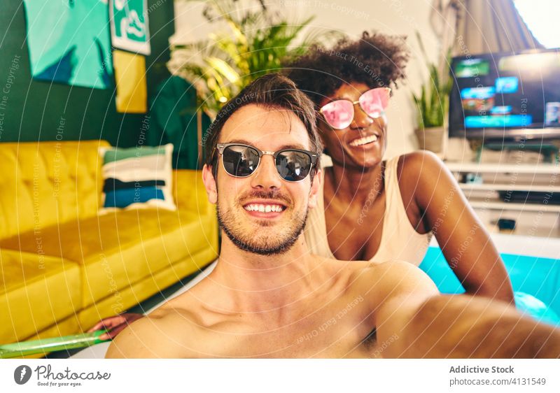 Smiling couple taking selfie during home party inflatable pool stay at home self isolation smile enjoy social distancing take photo having fun multiethnic