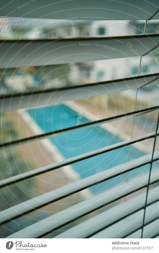 View of swimming pool through metal window blinds jalousie stay at home closed forbidden louvers water flat courtyard empty summer apartment aqua house