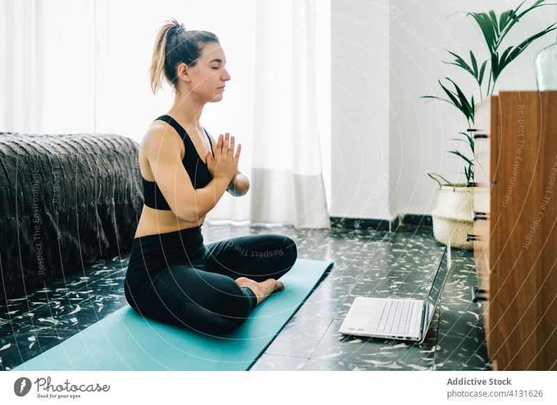 Young woman practicing yoga online at home meditate laptop lotus pose namaste calm young female gesture tutorial practice wellness asana device gadget lifestyle