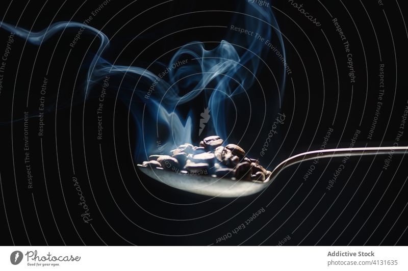 Metallic spoon with fresh coffee grains on black background view metal smoke steam up aroma dark room energy beverage caffeine delicious ingredient natural