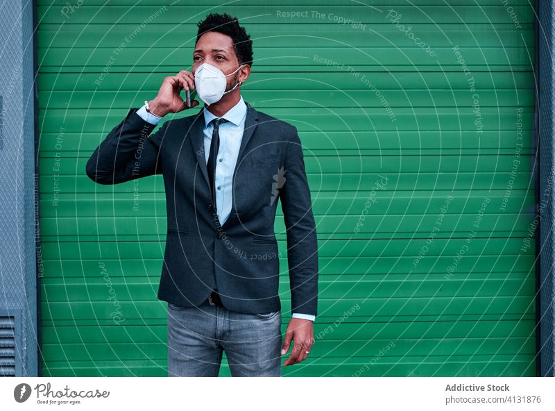 Serious ethnic businessman in respirator talking on smartphone on street phone call mask protect city pandemic infection virus entrepreneur coronavirus epidemic