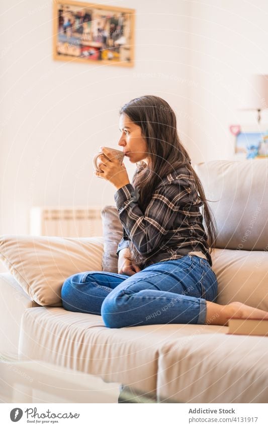 Young woman with cup of coffee resting on sofa home calm pensive young drink female casual cozy couch relax comfort lifestyle beverage sit chill thoughtful