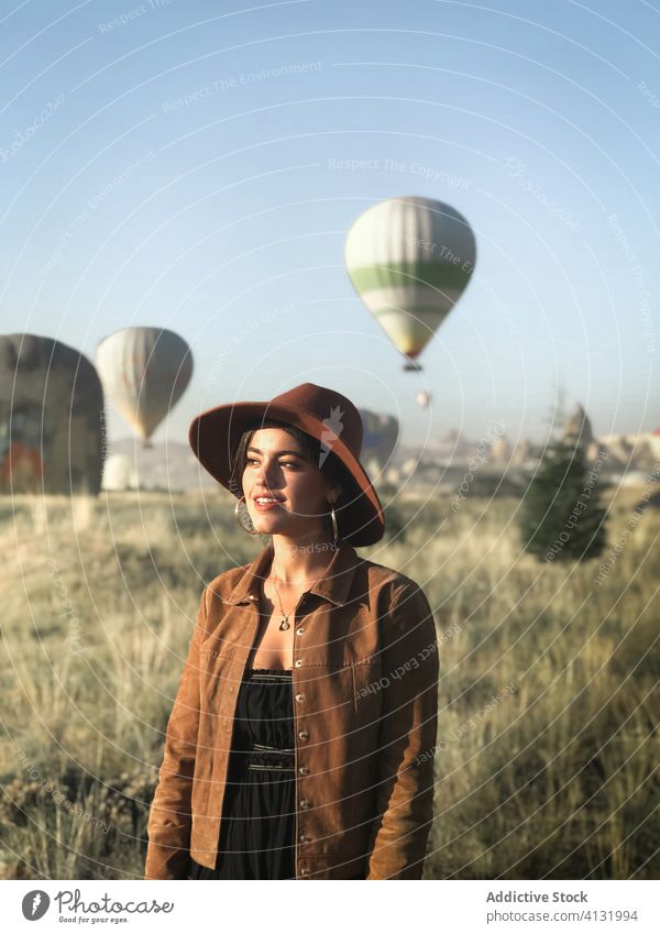 Traveling woman on background of hot air balloons in field travel tourist sunny trendy smile enjoy vacation female holiday nature green cheerful carefree trip