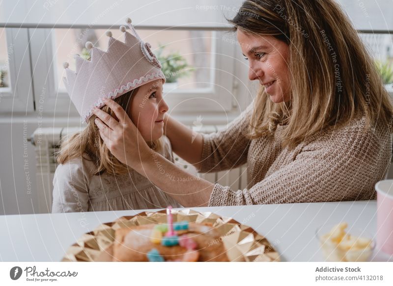 Mother putting decorative crown on daughter during holiday mother birthday princess love handmade party celebrate home felt kid event fun together girl parent