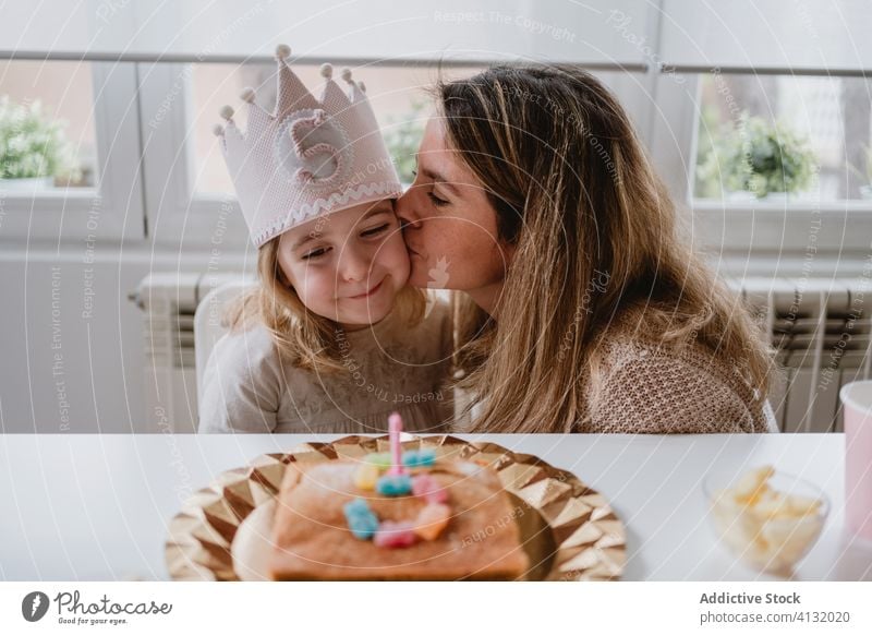 Happy mother kissing girl having birthday party brother celebrate happy together little excited home kid table positive parent child event love fun daughter
