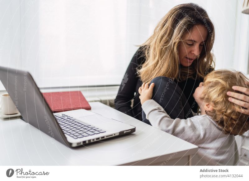 Busy woman kissing kid during online work at home mother laptop remote hug busy child embrace motherhood comfort interact parent casual young female love