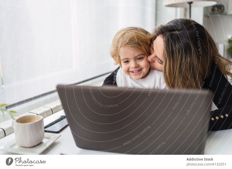 Woman with little kid working on laptop at home woman mother using together kiss online busy remote child curious motherhood interact parent female relationship