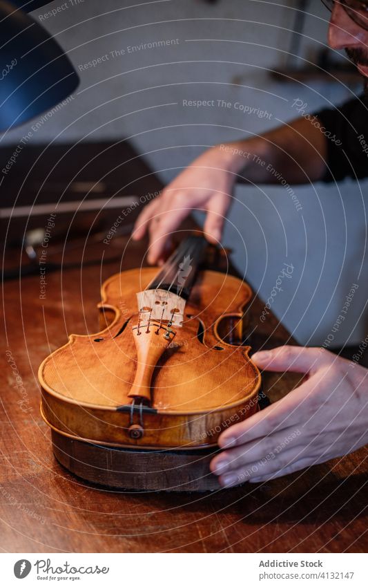 Crop craftsman adjusting strings of handmade violin in workshop artisan regulate sound person correctly workman soundboard skill acoustic process professional