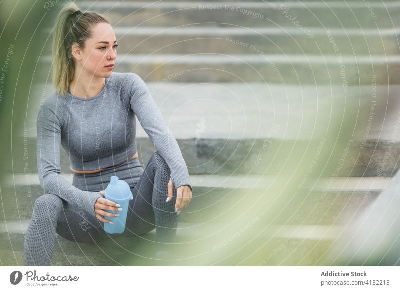 Contemplative sportswoman resting on stairs with bottle after workout athlete break water think contemplative healthy solitude fit peaceful sportswear wellbeing