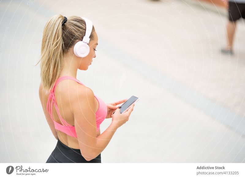 Sportive woman in headphones using social media on smartphone sportswoman sportswear listen music embankment sea gadget device internet online cellphone