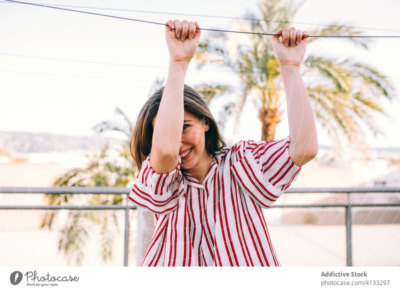 Cheerful woman in trendy blouse on balcony terrace playful style outfit smile having fun childish female rope summer positive apparel garment attire fashion