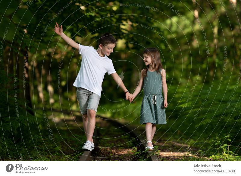 Content kids walking along abandoned railway in park brother sister together friendly smile green sibling friendship cheerful joy summer happy cute girl boy
