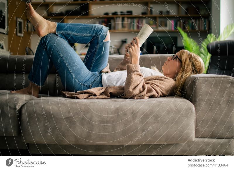 Thoughtful woman reading book in living room relax home thoughtful pensive interesting lying sofa female smart novel weekend cozy couch casual comfort story