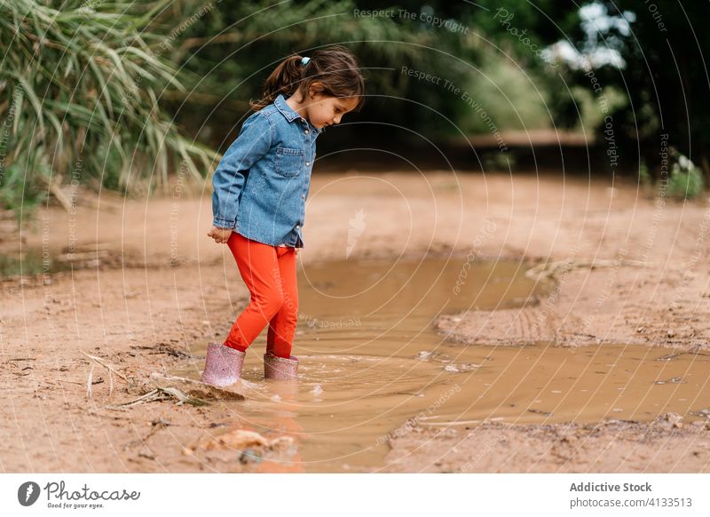 Curious girl playing in mud puddle child having fun weekend curious kid rubber boot cute dirty water wet adorable childhood joy activity rest playful ripple