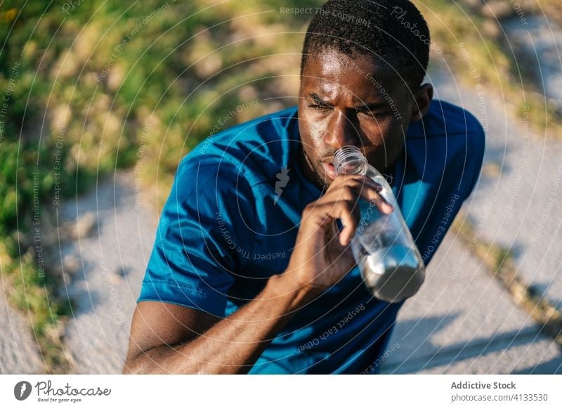 Athletic black man drinking water african fitness sitting down strong flexing body muscle biceps arms athlete strength lifestyle athletic training workout
