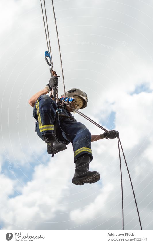 Fireman climbing down rope against cloudy sky firefighter training equipment fireman brave strong building practice male rescue complex workout uniform protect