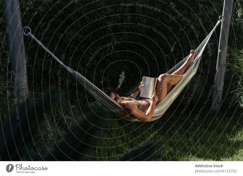 Relaxed woman with book resting in hammock relax chill summer read lying garden holiday vacation recreation lifestyle tranquil enjoy nature female young tan