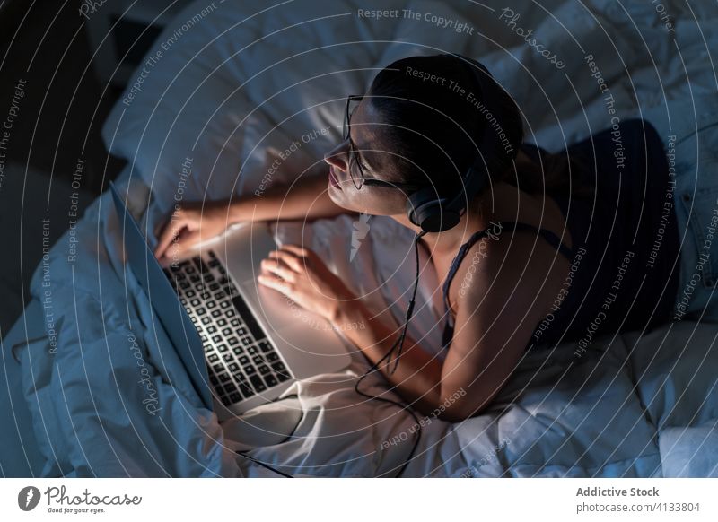 Woman listening to music with headphones in the computer on bed relax woman enjoy using song female browsing blanket lying down tank top device technology