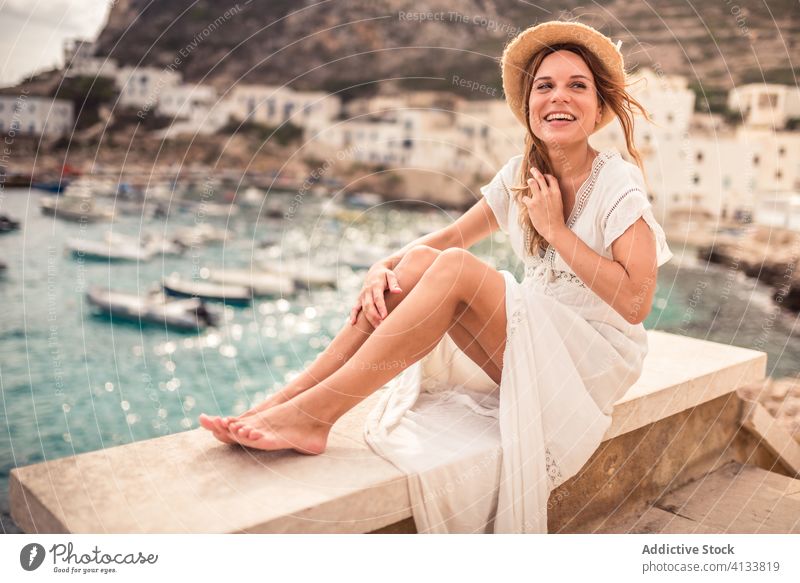 Delighted traveling woman on stone parapet in bay vacation harbor traveler delight tourist holiday boat female levanzo island summer happy fence smile sit