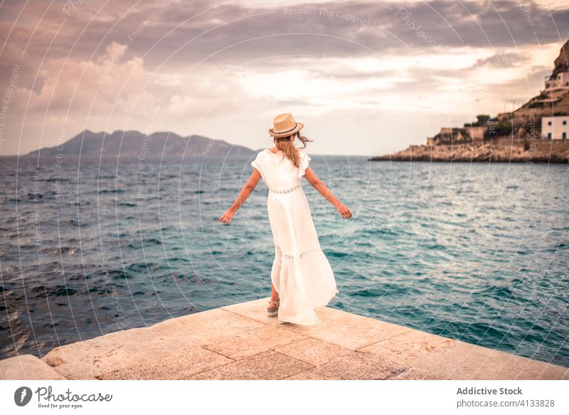Anonymous happy woman in dress and hat at seaside carefree travel seascape summer holiday seashore female levanzo island stone traveler vacation beach coast