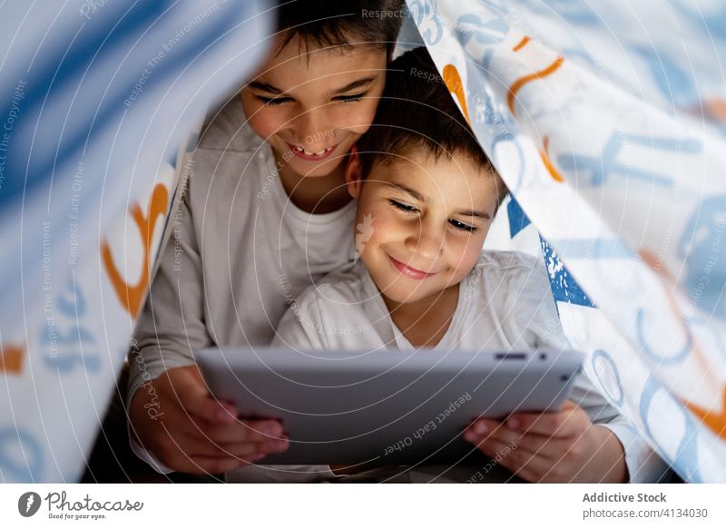 Happy brothers watching video on tablet together cartoon sibling browsing pajama blanket using hide enjoy home daytime interesting positive kid bed boy