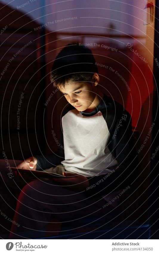 Child browsing tablet in evening kid using child device weekend entertain play online dark casual gadget home connection apartment internet rest relax childhood