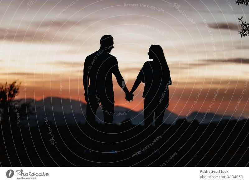 Young couple in love enjoying sunset in mountains romantic silhouette together sky twilight relationship holding hands evening affection tender travel freedom