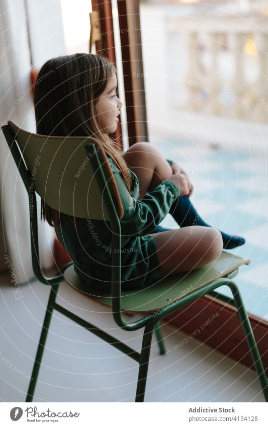 Dreamy girl sitting on chair near window thoughtful child observe relax street kid pensive dreamy calm home contemplate rest adorable cute think childhood