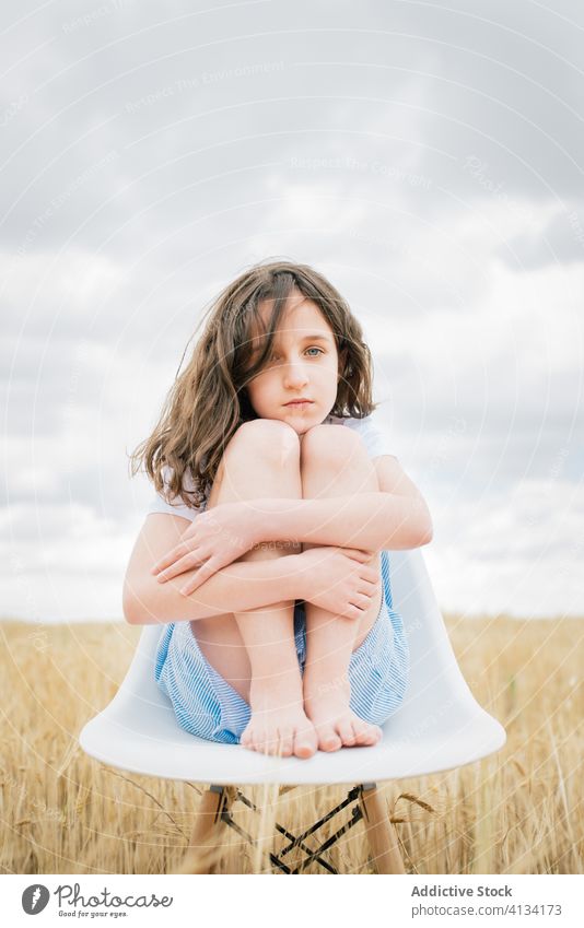 Lonely girl sitting on stool in field under cloudy sky lonely chair embrace knee barefoot concept cold autumn overcast solitude harmony melancholy childhood