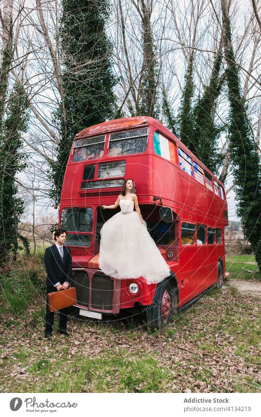 Couple of newlyweds near abandoned red bus in forest couple wedding double decker bride groom wood classy elegant wedding dress sit hood stand suitcase tuxedo