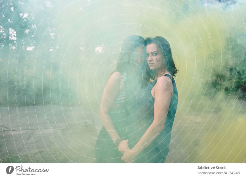 Sensual young lesbian couple standing in colored smoke sensual dreamy serene daydream yellow women head to head gay holding hands casual romance partner