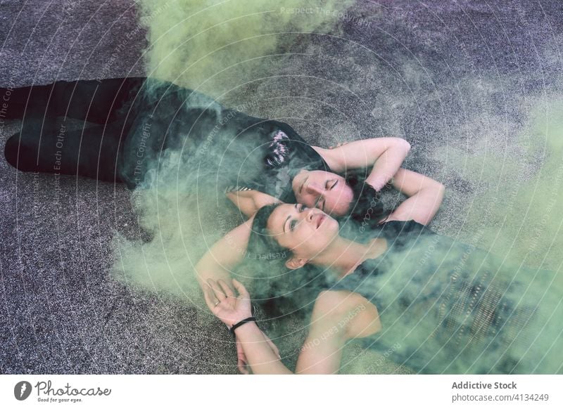 Sensual young lesbian couple lying in colored smoke sensual dreamy serene daydream yellow asphalt ground women head to head gay arms crossed casual romance