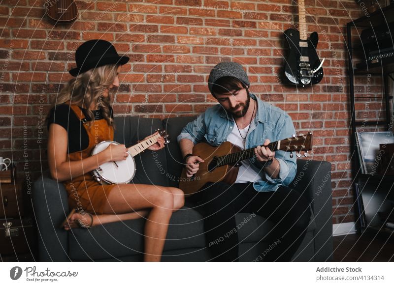 Cheerful couple playing guitar and banjo sitting on sofa music free time duet relationship friendship together legs crossed musical instrument boyfriend slim