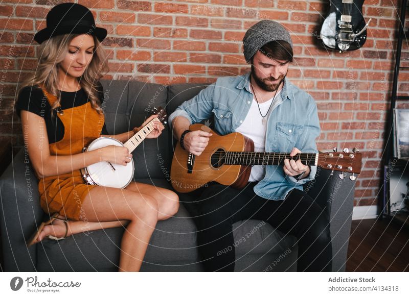 Cheerful couple playing guitar and banjo sitting on sofa music free time duet relationship friendship together legs crossed musical instrument boyfriend slim