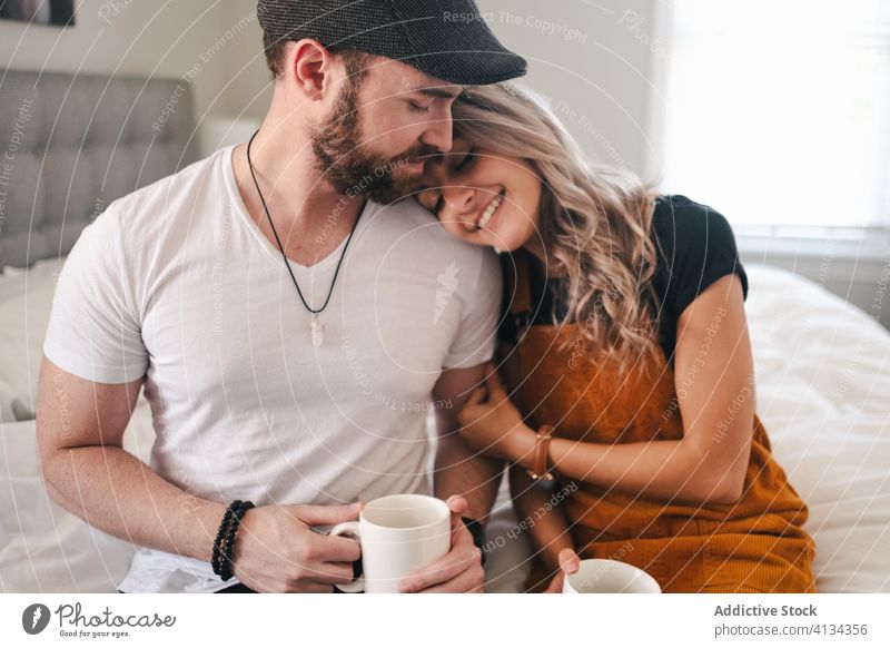 Happy couple embracing in bedroom while drinking coffee embrace hipster comfort mug cup relationship morning harmony love romance affection beverage breakfast