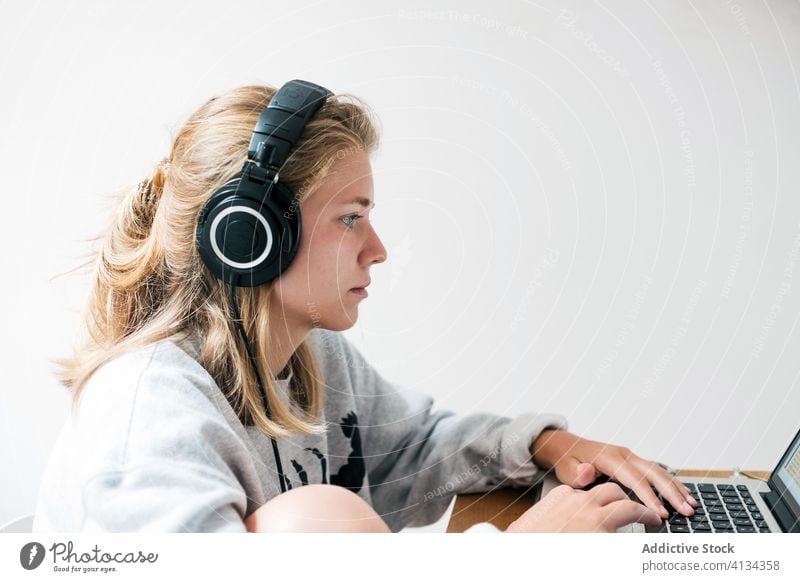 Young woman with headphones using laptop home gamer casual young browsing listen gadget serious focus device play computer lifestyle internet online modern