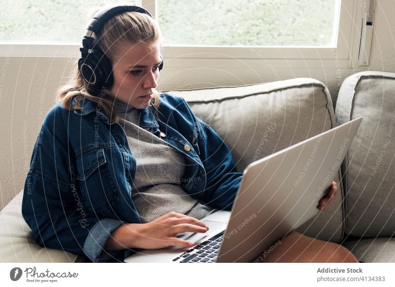 Modern woman working with laptop at home headphones sofa using focus concentrate young female casual wireless remote project freelance browsing device internet