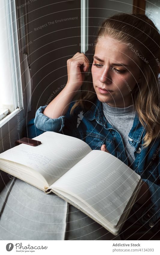 Pensive woman with notebook sitting near window diary home pensive young student notepad thoughtful read casual female think calm tranquil concentrate ponder