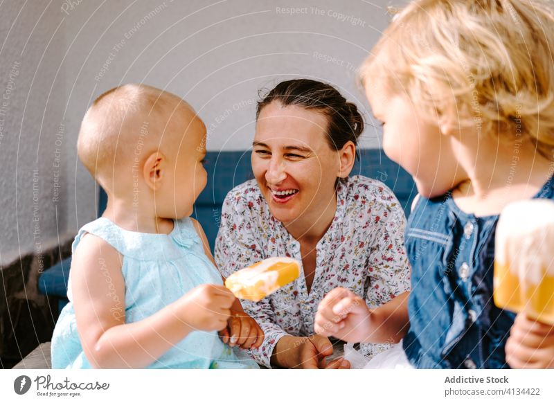 Delighted grandmother and little girls eating ice cream on terrace popsicle enjoy granddaughter together courtyard homemade delight woman cheerful toddler smile