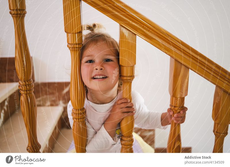Playful girl with head in stairway railings funny home stuck cute leisure playful step interior wooden pretty cheerful house staircase child kid rest casual