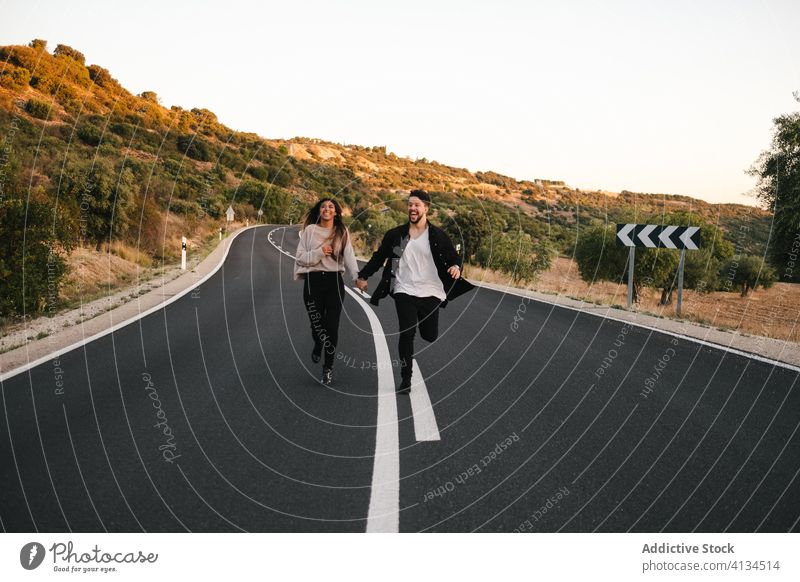 Carefree multiracial couple running along road freedom carefree mountain sunset together relationship holding hands multiethnic diverse roadway empty girlfriend