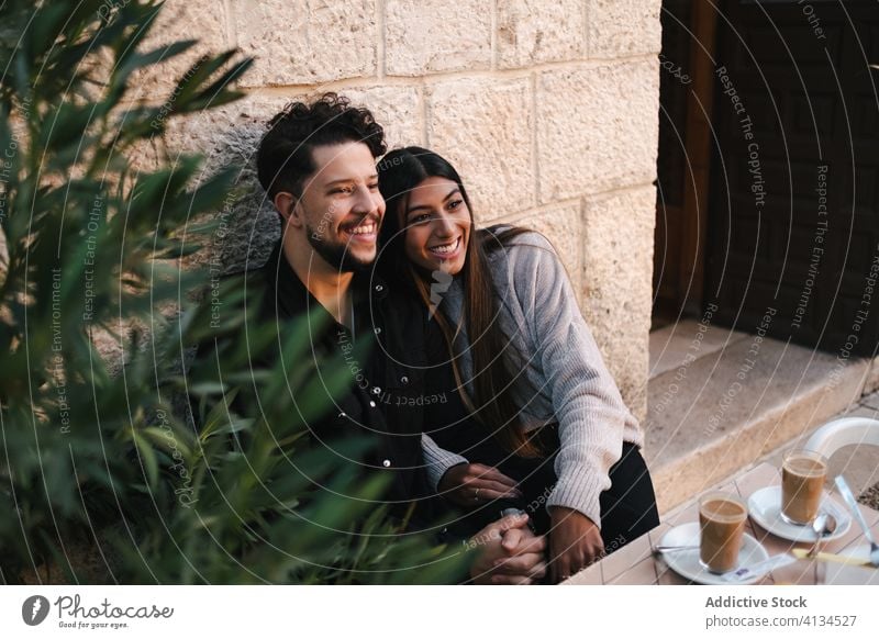 Content multiethnic couple sitting and laughing on street hug together cheerful stroll city having fun love multiracial diverse building aged stone windowsill