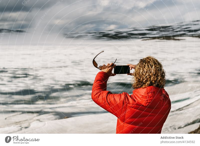 Traveling man taking photo of frozen lake travel take photo smartphone using tourist outerwear cold male iceland spectacular scenery vacation holiday sunny